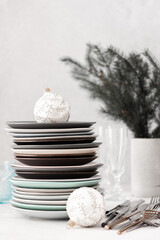 Preparing for a festive table setting, a stack of different plates and forks with knives, fir branches in a concrete vase, Christmas balls and decorations