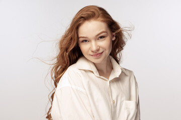 Charming redhead young girl with long curly hair looking at camera with light smile isolated on white background. Concept of youth, beauty, lifestyle