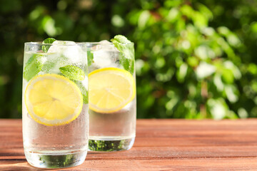 Fresh homemade citrus lemonade with lemons, mint and ice on a wooden table against greenery. Summer cold refreshing drinks. Selective focus, copy space