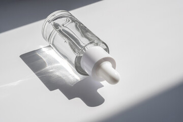 A white transparent bottle with serum in the rays of the sun.
