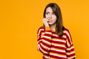 Young sad mistaken caucasian woman 20s in red striped sweatshirt look aside on workspace area mock up biting nails fingers isolated on plain yellow background studio portrait People lifestyle concept