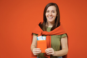 Traveler tourist woman wear khaki t-shirt sweatshirt hold passport boarding tickets isolated on plain orange background studio. Passenger travel abroad on weekends getaway. Air flight journey concept.