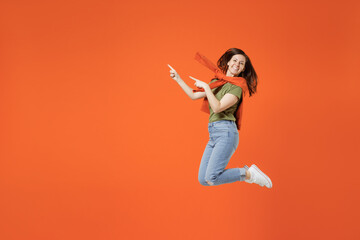 Fototapeta na wymiar Full body side view young happy woman in khaki t-shirt tied sweater on shoulders look camera point index finger aside on workspace area isolated on plain orange background. People lifestyle concept.
