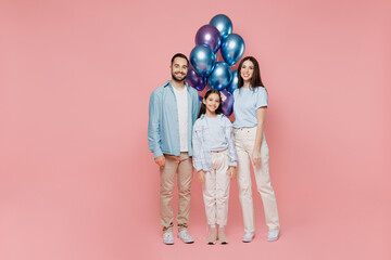 Full body young parents mom dad with child kid daughter teen girl in blue clothes celebrating birthday holiday party hold bunch air inflated helium balloons isolated on plain pastel pink background