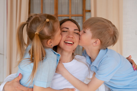 Tender loving mother with son and daughter, children kids hug mom and kiss her from both sides in cheeks, friendly happy family at home spending time leisure. Medium shot. Smiling emotionally