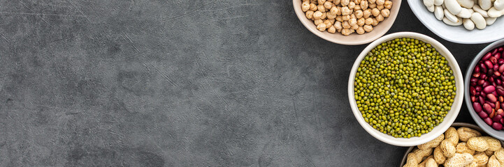 Banner of different types of legumes in bowls, green peas and chickpeas , colored beans and maash and peanuts, top view, copy space