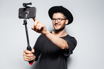Fototapeta na wymiar Young happy man making photo by smartphone with selfie stick on grey background.