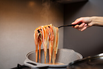 Close-up of female hand holding a spoon with pasta above pot on kitchen stove.
