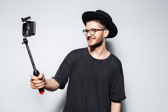 Young happy man making video by smartphone with selfie stick on grey background.