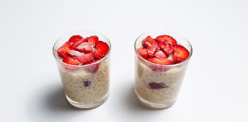 Close-up of two cups of vegan dessert, pudding with strawberries on white.