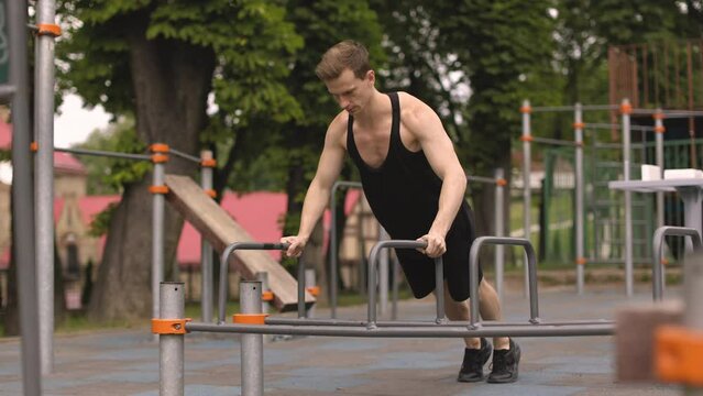 Handsome caucasian sports man doing push up exercise on parallel bars at outdoor gym, home workout in the open air concept.
