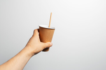 Male hand holding paper cup of coffee with bamboo straw on white.