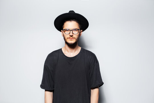Studio portrait of young serious man wearing black hat and glasses on white.
