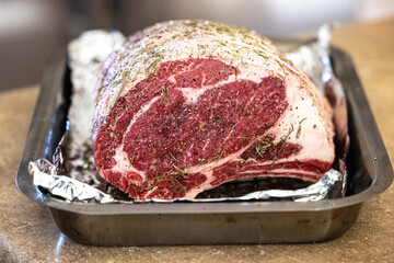 Raw prime rib roast seasoned and sitting on an aluminum foil lined pan ready for the oven for a...