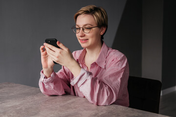 Smiling young woman using smartphone indoors. Girl looking at mobile phone sitting in office