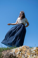 A girl in a dress sits on the shore of a blue lake in summer