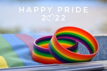  'Happy PRIDE 2022', and rainbow wristband, symbol of lgbt, on blurred rainbow flags background, concept for lgbtq+ celebrations in pride month, june, around the world.