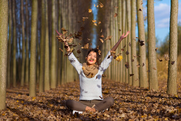 Beautiful smiling girl throws dry forest leaves in the air on a sunny autumn day