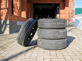 A new set of summer tires stacked on the sidewalk in the yard. Car tires on steel rims are ready for seasonal replacement.