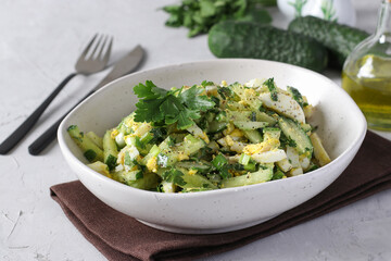 Salad with squid, cucumber, egg and green onion dressed with olive oil in a white bowl on light gray background