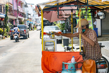 Obraz na płótnie Canvas A man with a mobile kitchen on a cart by a motorcycle offers food on the street, Bangkok, Thailand.