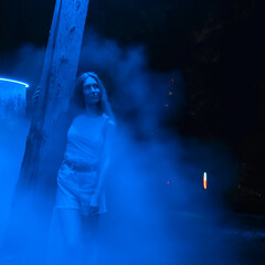 A woman stands hugging a tree trunk in a mystical blue haze at night. Blurred image