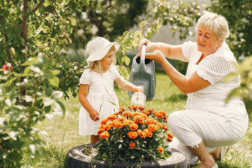Little girl and her grandmother watering flowers in garden