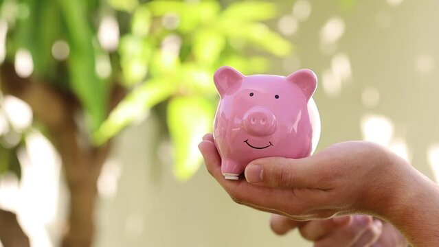 Dinheiro, Real Brasileiro. Um homem jovem segurando um cofrinho e colocando moedas do Real Brasileiro - BRL. Conceitos de guardar dinheiro e investimentos.