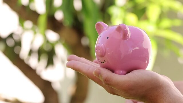 Dinheiro, Real Brasileiro. Um homem jovem segurando um cofrinho e colocando moedas do Real Brasileiro - BRL. Conceitos de guardar dinheiro e investimentos.