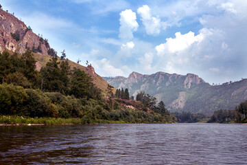 A river and forested mountains along its banks. Summer landscape. Travel, hiking, healthy lifestyle.