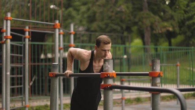 Fit man doing triceps dips on parallel bars at park exercising outdoors. Beautiful man doing work out and different exercises outdoor.
