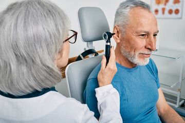 Senior man during ear test with audiologist at audiology. Diagnosis of impairment and hearing testing to senior people, otoscopy
