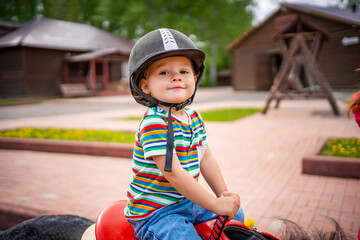 Beautiful little girl two years old riding pony horse in big safety jockey helmet posing outdoors...