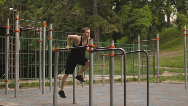 Young caucasian sporty muscular fit man doing triceps dips on parallel bars at an outdoor gym park. Attractive man warming up.