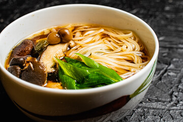 Mushroom soup udon noodles with fresh green onions in a fine white bowl against a black design board, a traditional Japanese meal.