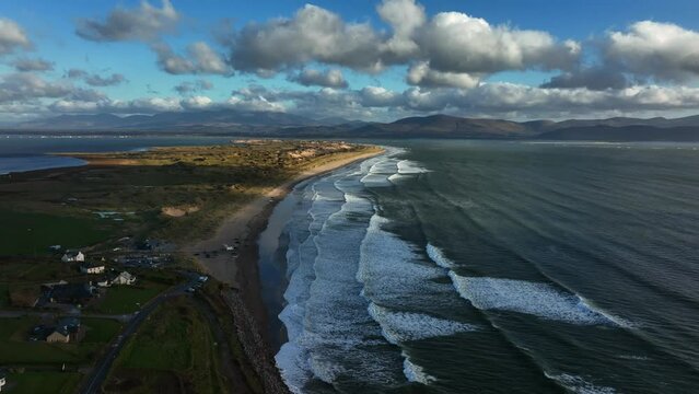 Inch Beach, Kerry, Ireland, March 2022. Drone gradually orbits from the northwest at a high altitude as waves crash along the coast on Dingle Bay with Killorglin and Killarney in the distance.