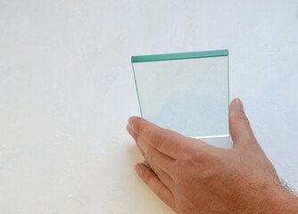 male hand holding glass sample, transparent glass in hand on white background, industrial glass