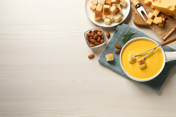 Pot of tasty cheese fondue, bread and almonds on white wooden table, flat lay. Space for text