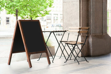 Blank wooden sandwich board near chair and table outdoors. Mockup for design