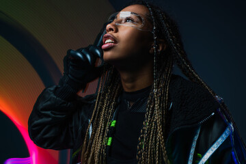 Naklejka premium Stylish african american woman in cyber glove and smart glasses standing on grey background with abstraction.