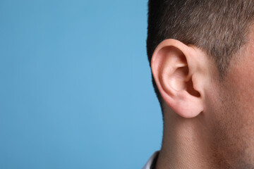 Obraz premium Man on light blue background, closeup of ear. Space for text