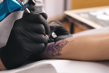 Professional artist making tattoo on hand in salon, closeup