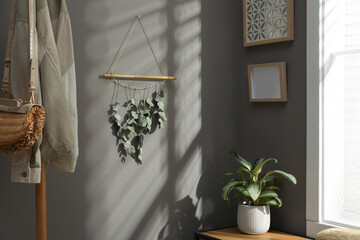 Beautiful decor element made of dry bamboo stick and eucalyptus branches hanging on grey wall in...