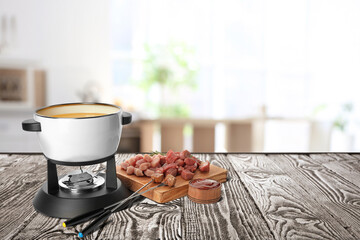 Composition with fondue pot and meat on wooden table in kitchen. Space for text