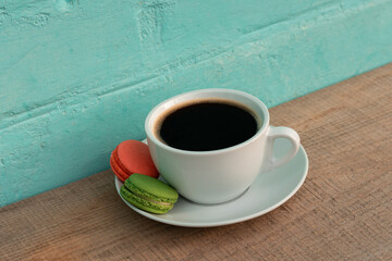 Cup of black coffee with green and red macaroons on wooden table