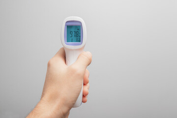 Hand with infrared digital non-contact thermometer. Display shows the normal body temperature. An outbreak of a coronavirus epidemic or monkey pox.