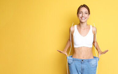 Happy young woman with slim body in oversized jeans on yellow background, space for text. Weight...