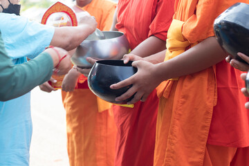 Young Buddhist monks or novice monk are given food, drinking water,banknotes offerings from people.