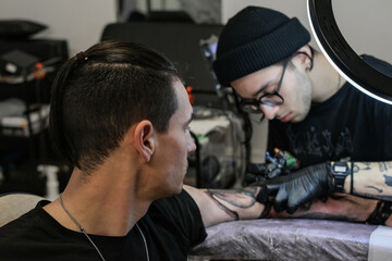 Professional tattoo artist stuffs a tattoo on the man's hand. Tattoo artist at work. Tattoo creation process. Art and creativity