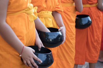 Novice monks hold alms bowls waiting for people to offer food to monks in the morning in Thailand.
